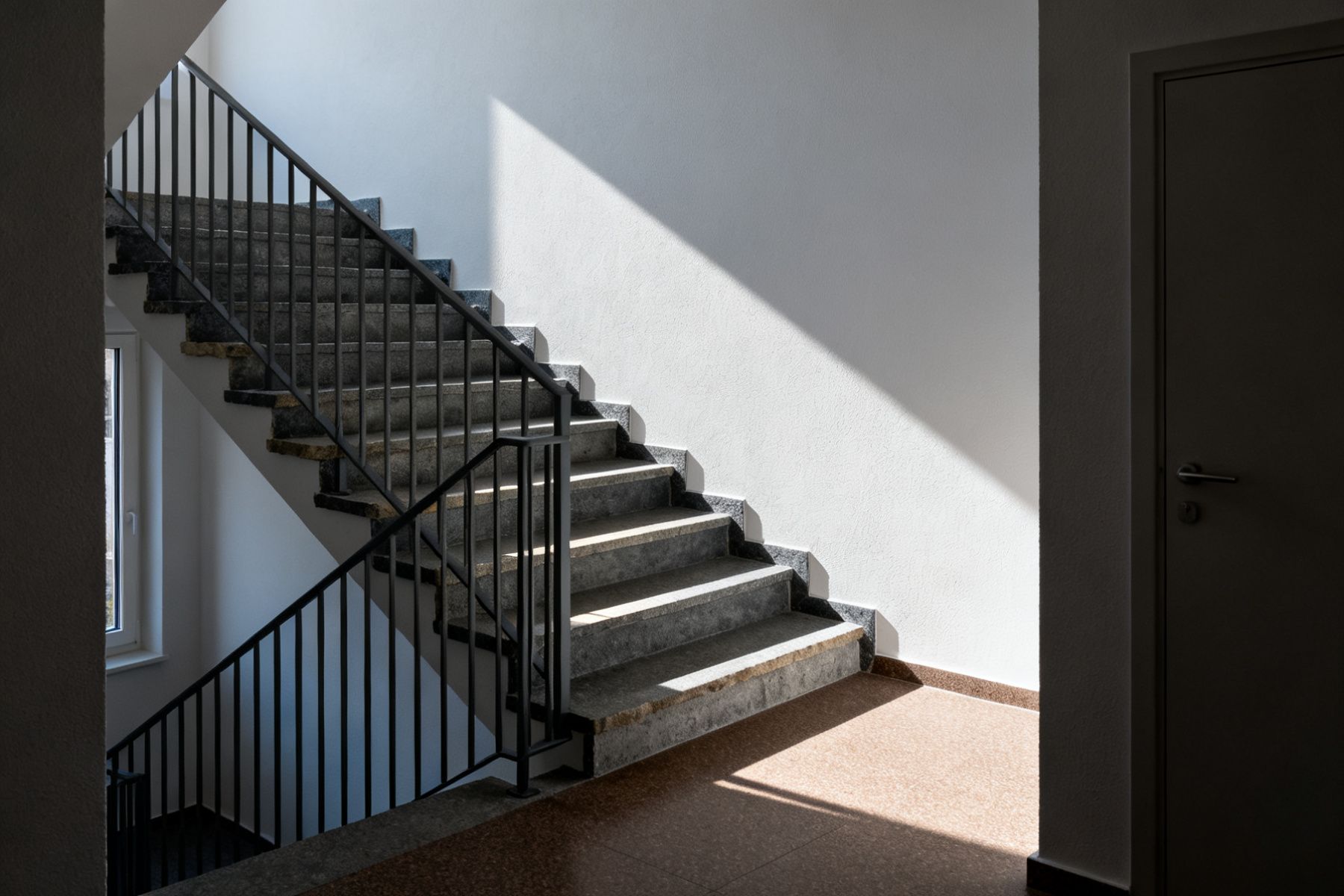 Treppenhaus eines Wohnhauses am frühen Morgen, geschlossene Wohnungstür im Halbdunkel